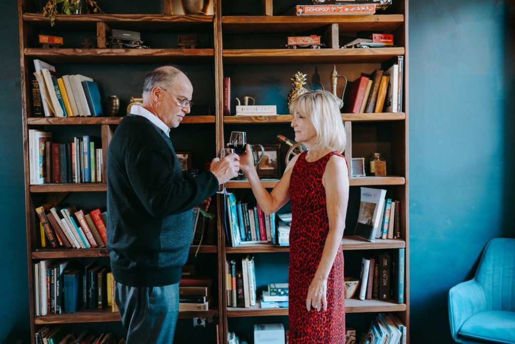 Man in a navy sweater sharing a toast with his partner in front of a home library