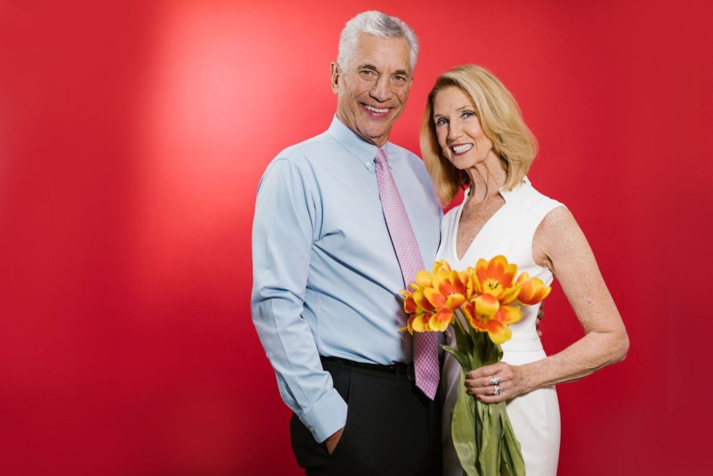 Silver-haired man in a blue shirt and tie beside his partner holding orange tulips