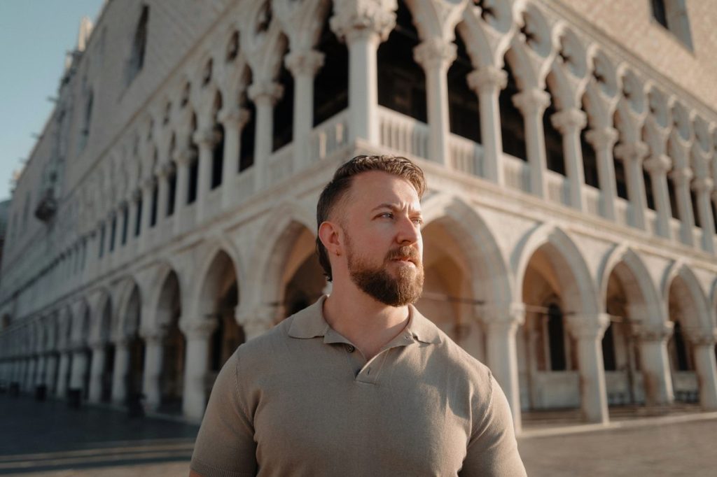 Man in a polo shirt in front of a historic arcaded palace while traveling, illustrating choosing between testosterone injections, pellets and cream
