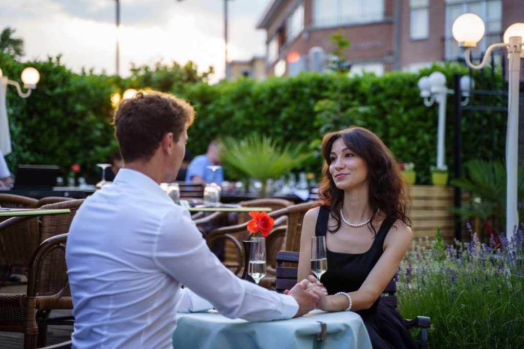 Couple holding hands at dinner on a garden restaurant terrace, illustrating choosing a testosterone option together