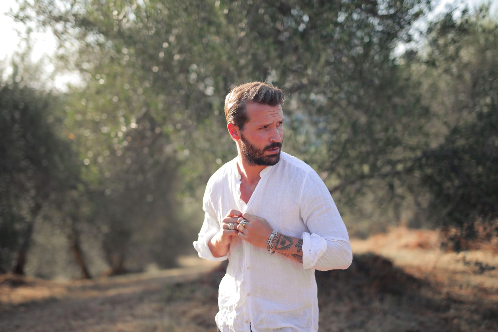 Testosterone pellets vs injections: bearded man in a white linen shirt in a sunny olive grove