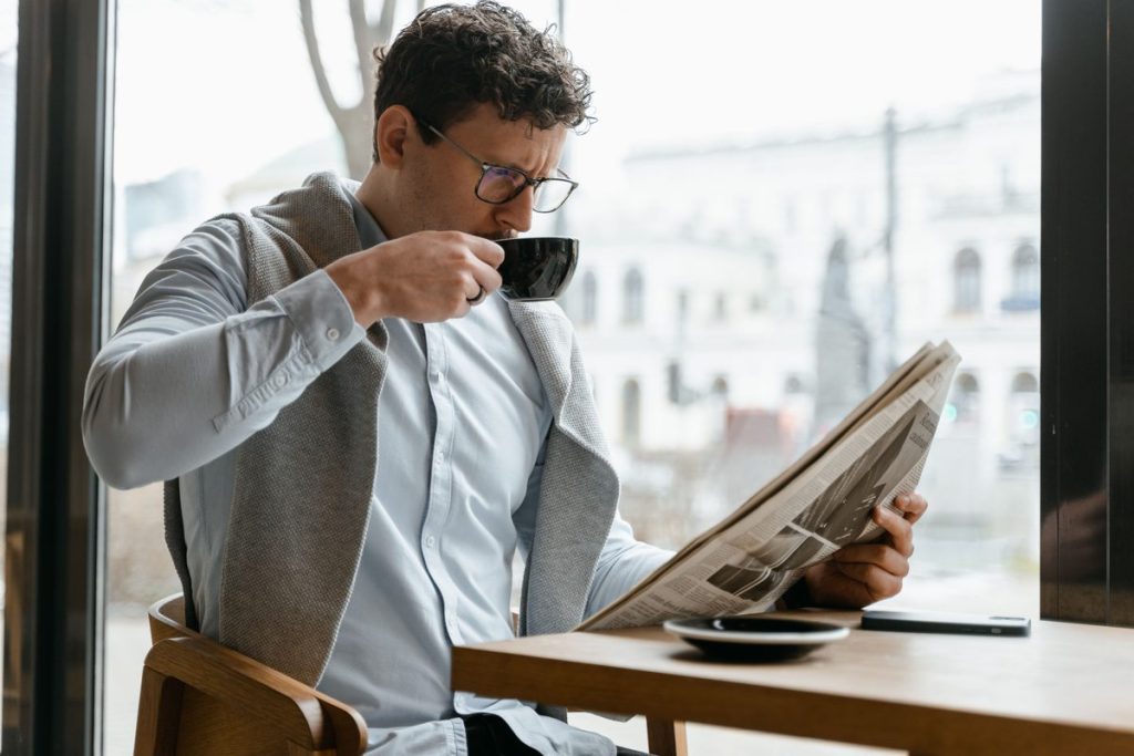 Man in glasses reading the newspaper over coffee in a bright café, illustrating using HSA or FSA funds for testosterone therapy