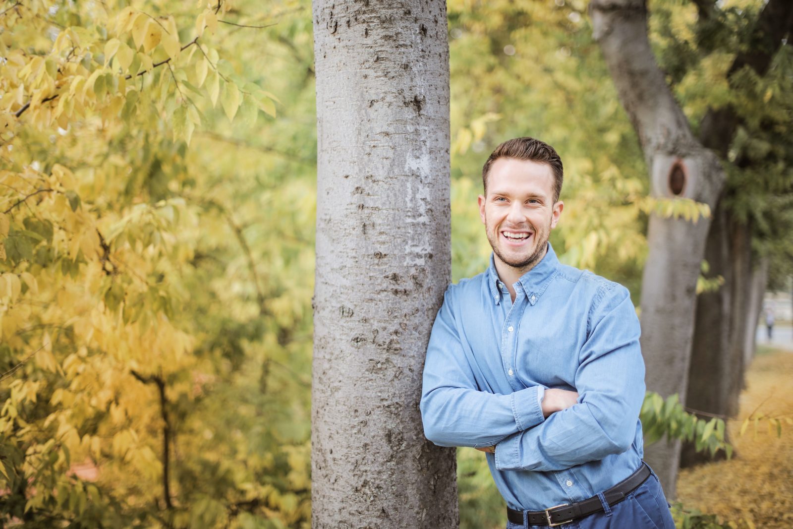 TRT Schaumburg: smiling man in a light blue shirt leaning against a tree in an autumn park